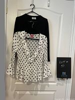 Black wool sweater and black & white polka dot top hanging on a door, showing full front view of both items