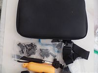 Black carrying case with various action camera mounting accessories including clips, brackets, straps, and a yellow floating handle grip.