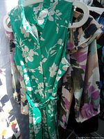 Close-up photo of green floral sleeveless shirt dress with white flower print, button front and waist tie, on a hanger