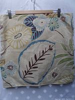 Close-up of one pillow cover showing tropical floral pattern in blue, green, brown on natural linen-color fabric.