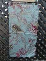 A piece of aqua blue cotton fabric with pink floral pattern, shown hung up to display print detail and texture.