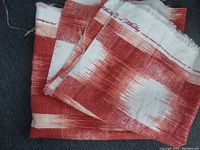 Close-up image of folded orange/red Ikat patterned fabric with visible selvedge text 'Raleigh Ikat Plaid' by Williamsburg.