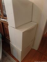 Five stacked, white, narrow plastic storage bins with a curved front, typical of Ikea wall-mounted designs, showing light use.