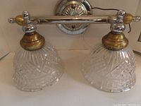 Full view of vanity light fixture showing chrome and gold fixture with two cut-glass bell-shaped shades