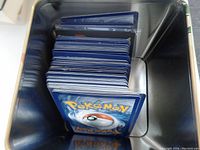 Top view of metal tin filled with stacked Pokemon cards showing card backs with Pokeball design.