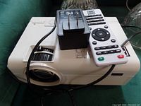 Top view of RCA white projector with AC adapter and remote control resting on top