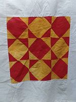 Close-up photo of a single yellow and red quilt block with a geometric pattern, hand-stitched fabric with some discoloration.