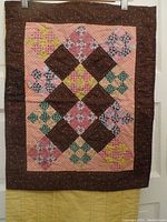 Brown hand-quilted placemat with geometric and floral patchwork on pink background and brown polka dot border