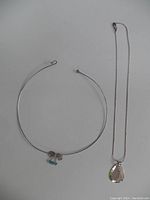 Two silver necklaces displayed on a white surface, one a wire choker with beads, the other a chain with pendant.