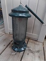 Full view of the green metal mesh Squirrel Buster bird feeder with four metal feeding ports and attached hanging hook.