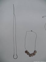 Two sterling silver necklaces laid flat on a white background. The shorter necklace has five round discs attached, tarnished and needing cleaning. The longer necklace has a simple horseshoe pendant.