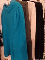 Five sweaters hanging on a rack, colors turquoise, tan, off-white, and black visible.