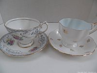 Two bone china teacups on their matching saucers, showing floral patterns and gold trim.
