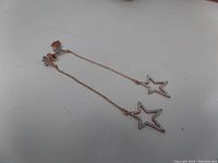 Pair of rose gold-plated silver chain earrings with star-shaped pendants hanging from post backs on a white surface.
