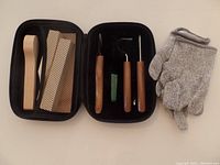 Whittling tools in black zippered case including carving tools, wooden spatulas, abrasive paper, sharpening stone, and protective glove.