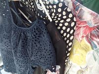 Four women's blouses hanging, various styles and colors including navy eyelet, polka dots, floral prints