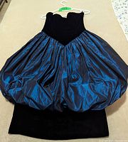 Front view of a strapless 1980s prom dress with a fitted black velvet bodice and voluminous shiny blue bubble skirt on a hanger.