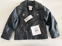 Toddler size 2T black vegan leather jacket with original tags and front zipper, showing the style and condition of the item.