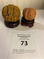 Two walnut carvings on wood stands with auction lot number card for scale and identification.