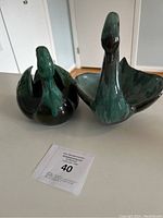 Front view of two ceramic swan figurines with green and black glaze, sitting on a table with a tags showing auction number 40.