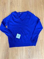 Full view of the medium blue V-neck cashmere sweater lying flat on a wooden floor with a tag.