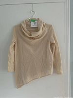Front view of the beige cashmere sweater with cowl neck and asymmetrical hem
