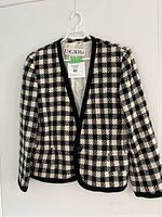 Full front view of vintage Escada blazer hanging on a white hanger, showing black and white checkered pattern and black trim edges with one button.