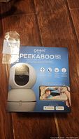 Front box image showing Geeni Peekaboo HD baby monitor with camera and a parent viewing a baby on a mobile device.
