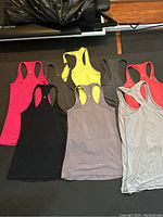Eight Lululemon racetrack style workout tank tops laid out flat showing front side, assorted colors including pink, black, yellow, gray, red and striped gray.