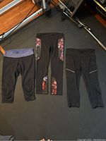 Three pairs of black Lululemon yoga pants laid flat on floor showing different design details.