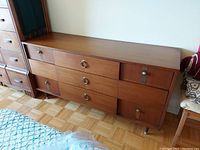 Photo of wood Mid-Century Modern style dresser with multiple drawers and metal ring handles.