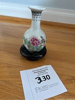 Porcelain bud vase with flower and bird painted on front, placed on wooden stand.