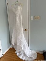 Full view of the white strapless wedding dress with a long train hanging on a door.