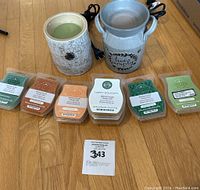 Photo showing two Scentsy wax warmers (birch bark and milk can styles) with seven packs of various scented wax melts laid out in front of them on a wooden floor.