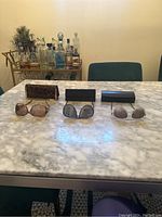 Three pairs of sunglasses displayed on marble table with their respective cases behind them