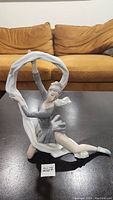 Full view of the NAO porcelain figurine showing the dancer kneeling with veil above her head on a dark surface, brown couch background.