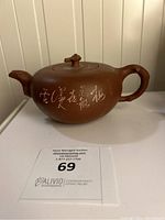 Front side view of brown clay teapot showing dragon head spout and body inscription