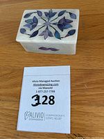 Photo of closed rectangular marble trinket box showing top floral inlay design with mother of pearl and stones in purple and blue hues.