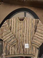 Full view of the multicolored textured knit sweater laid flat on a glass table, showing ribbed neckline, cuffs, and hem.