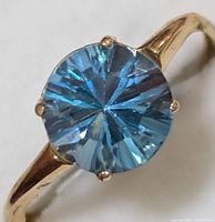 Close-up front view of ring with round blue topaz and yellow gold band