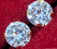 Close-up view of two round clear cubic zirconia stones set in 14K gold prong settings on a red background.