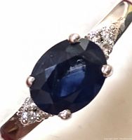 Close-up oblique top angle showing oval blue sapphire and diamond accents on white gold band.