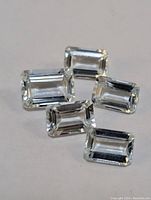 Five emerald cut aquamarine gemstones placed on a white background, showcasing their clarity and light blue color.