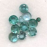 Eleven small round faceted green emerald gemstones laid out with visible internal inclusions and color variations.