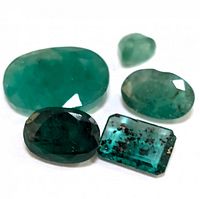Five emerald gemstones displayed on a white background showing size and color variation with visible inclusions in some stones.