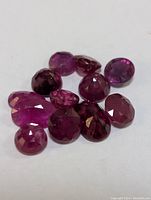 Top view of eleven loose, faceted genuine rubies of varied shapes and sizes on a white background.