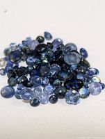 Pile of assorted genuine sapphire gemstones in various cuts and shades of blue on white background.