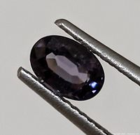 Close-up photo of dark blue oval faceted sapphire held by tweezers showing good clarity and cut.