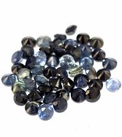 Close-up image showing approximately 40 loose, faceted round sapphires in shades of blue and greenish hues on white background.