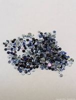 Loose genuine sapphire gemstones in varying shades of blue and some multicolored hues scattered on a white surface.